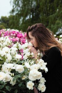 Yound woman in rose garden smelling white roses