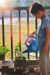 Young boy watering potted plants on porch